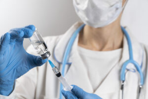 A doctor in a white coat, medical mask and protective gloves takes medicine from a glass ampoule into a syringe. The vaccine is in the hands of a nurse. The concept of treatment and prevention of the spread of covid-19 infection, virus and pneumonia.