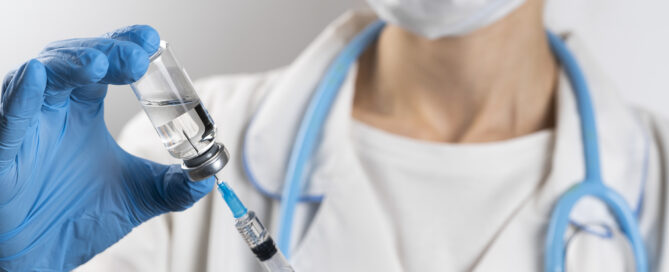 A doctor in a white coat, medical mask and protective gloves takes medicine from a glass ampoule into a syringe. The vaccine is in the hands of a nurse. The concept of treatment and prevention of the spread of covid-19 infection, virus and pneumonia.
