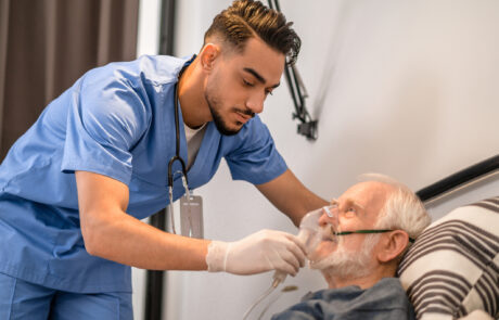 Calm focused young medical worker putting on an oxygen mask on the aged male patient
