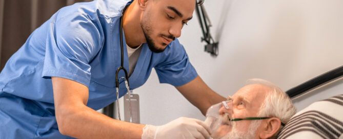 Calm focused young medical worker putting on an oxygen mask on the aged male patient