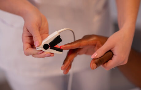 Female physician stands by an African patient, checking his blood oxygen with a pulse oximeter in the hospital ward.
