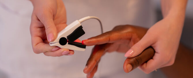 Female physician stands by an African patient, checking his blood oxygen with a pulse oximeter in the hospital ward.